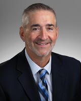 Jerome Guanciale in black suit, white shirt, and tie with blue design.